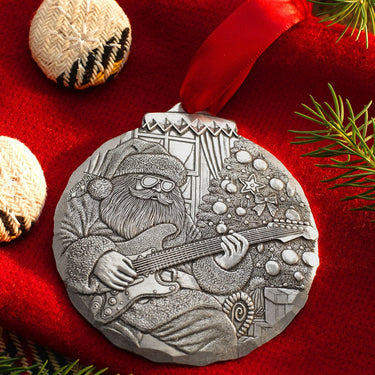 Silver ornament with a design of a person playing guitar on a red background with Christmas decorations.