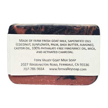 Bar of Handmade goat milk soap with activated charcoal with a label detailing ingredients and contact information on a white background