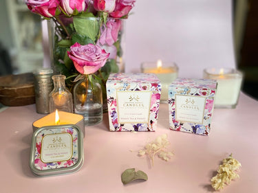 Rose of Sharon Soy Lotion Candle with floral packaging on a table with flowers and candles in the background