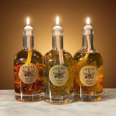 Three lit oil lamps made from glass bottles labeled 'Hesita', 'Selene', and 'Helios' on a marble surface.