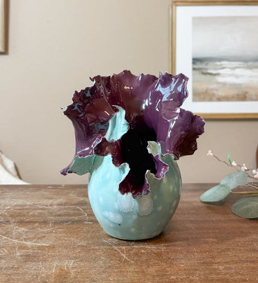 Teal vase with purple flowers on a wooden surface
