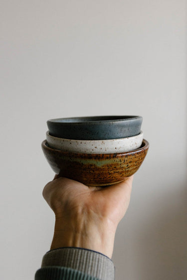Hand holding a stack of three ceramic bowls against a plain background