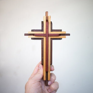 Wooden cross-shaped object held by a hand against a light gray background