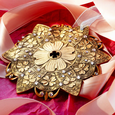 Decorative gold brooch with floral patterns on a pink ribbon background