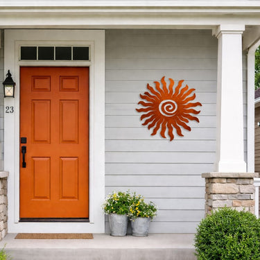 Orange front door with decorative sun design on a gray house exterior.