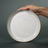 Hand holding a ceramic plate against a gray background