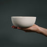 Hand holding a white ceramic bowl against a dark background