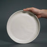 Hand holding a white ceramic plate against a dark background