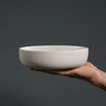 Hand holding a white ceramic bowl against a dark background