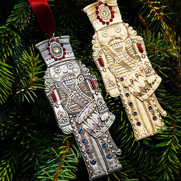 Two decorative nutcracker ornaments, one silver and one gold, on a Christmas tree.