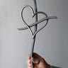Hand holding a metal Promise Cross with an interlocking heart against a steel gray background