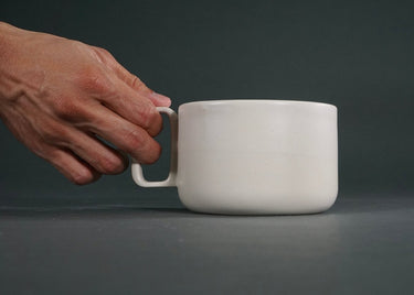 White ceramic mug with a hand holding its handle against a dark background