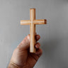 Hand holding a wooden cross against a gray background