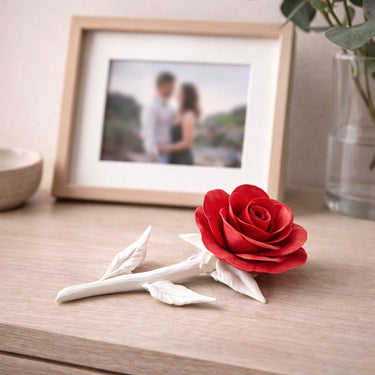 Red ceramic rose on a wooden surface with a framed photo in the background