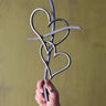 Hand holding a metal decorative cross with heart shapes against a yellow background